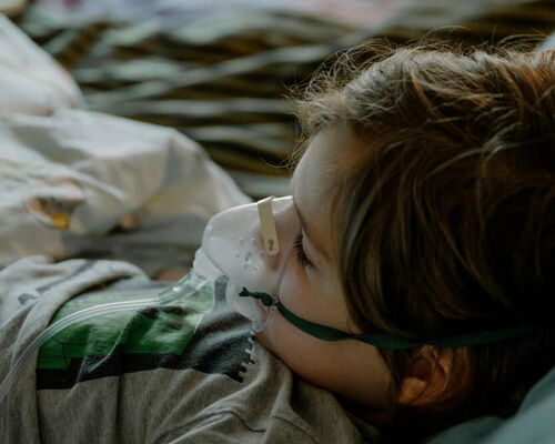 ein Junge liegt mit Sauerstoffmaske im Bett