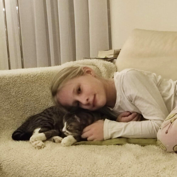 Amelie liegt müde mit einer Katze im Pyjama auf dem Sofa