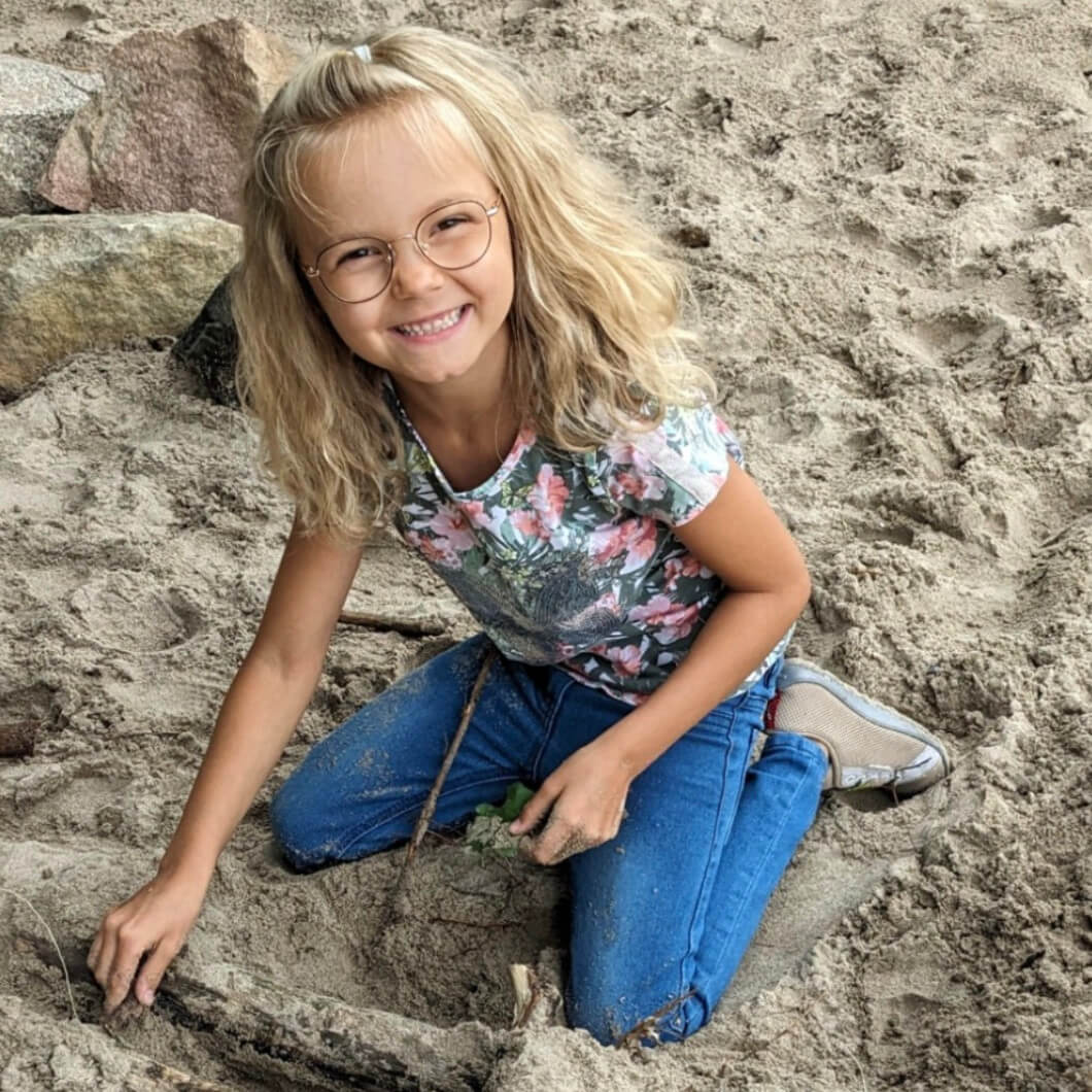 Annabelle vor ME/CFS. Sie hockt fröhlich lächelnd im Sand