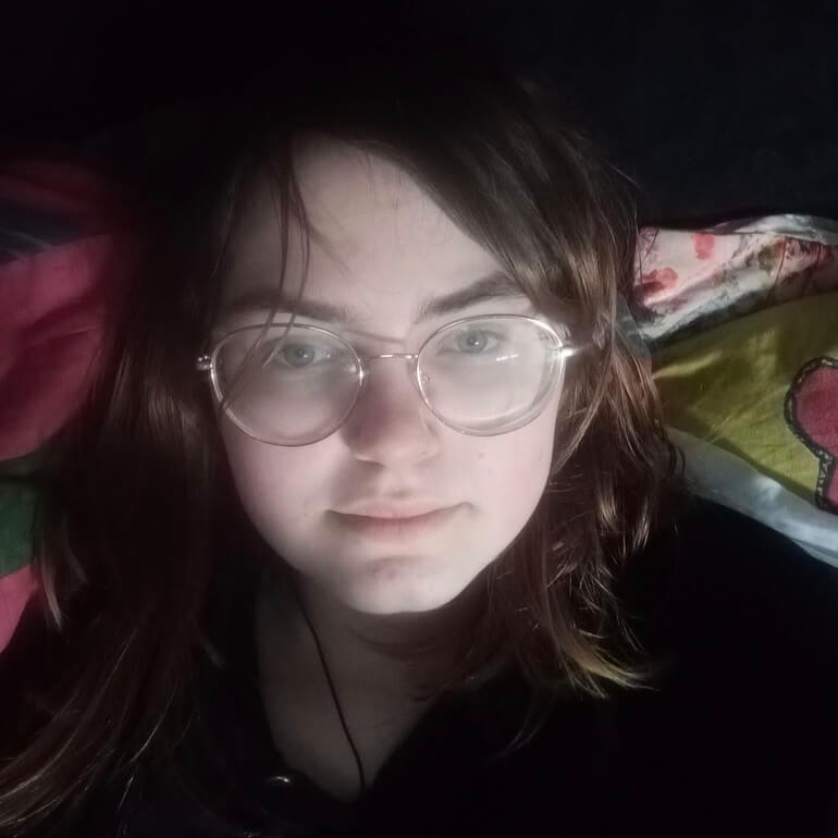 Aurora liegt mit ME/CFS im Bett und schaut in die Kamera, sie ist sehr blass
