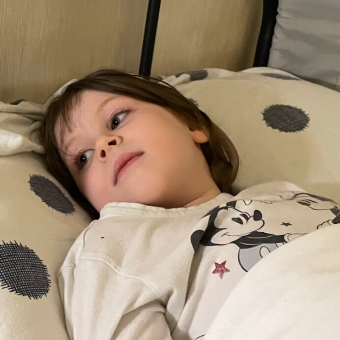 Elin mit ME/CFS. Sie liegt im Micky Maus Pyjama im Bett und schaut zur Seite.