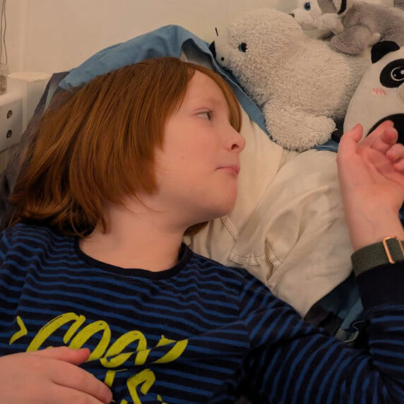 Emil mit ME/CFS. Er liegt im Bett und schaut zu seinen Kuscheltieren.