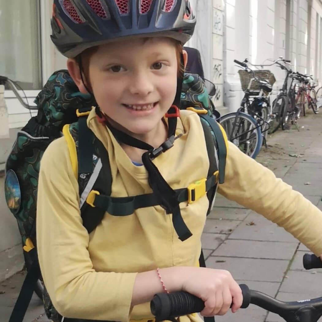 Emil vor der Krankheit. Er steht lächelnd mit Helm und den Händen am Lenkrad eines Rollers