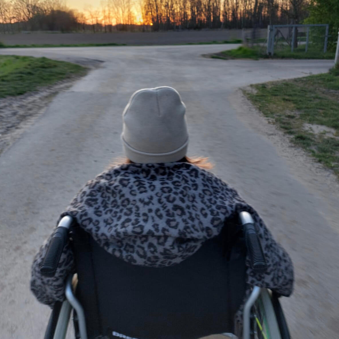 Greta mit ME/CFS von hinten im Rollstuhl sitzend; sie fährt eine Straße entlang