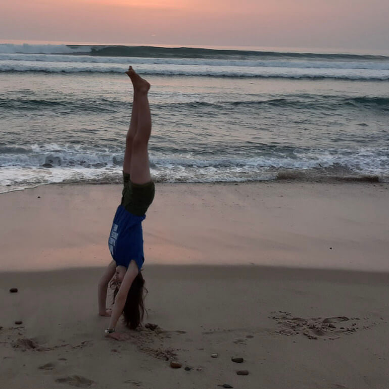 Juliane macht Handstand am Strand, im Hintergrund das Meer