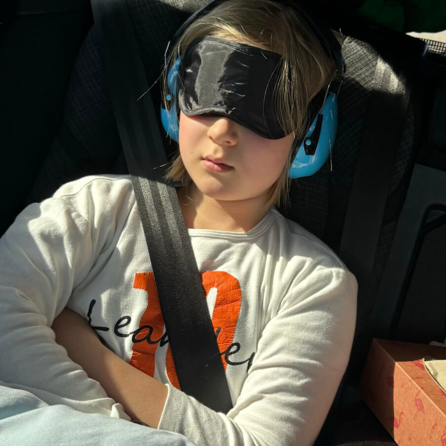 Leander sitzt Augenmaske und Hörschutz im Auto