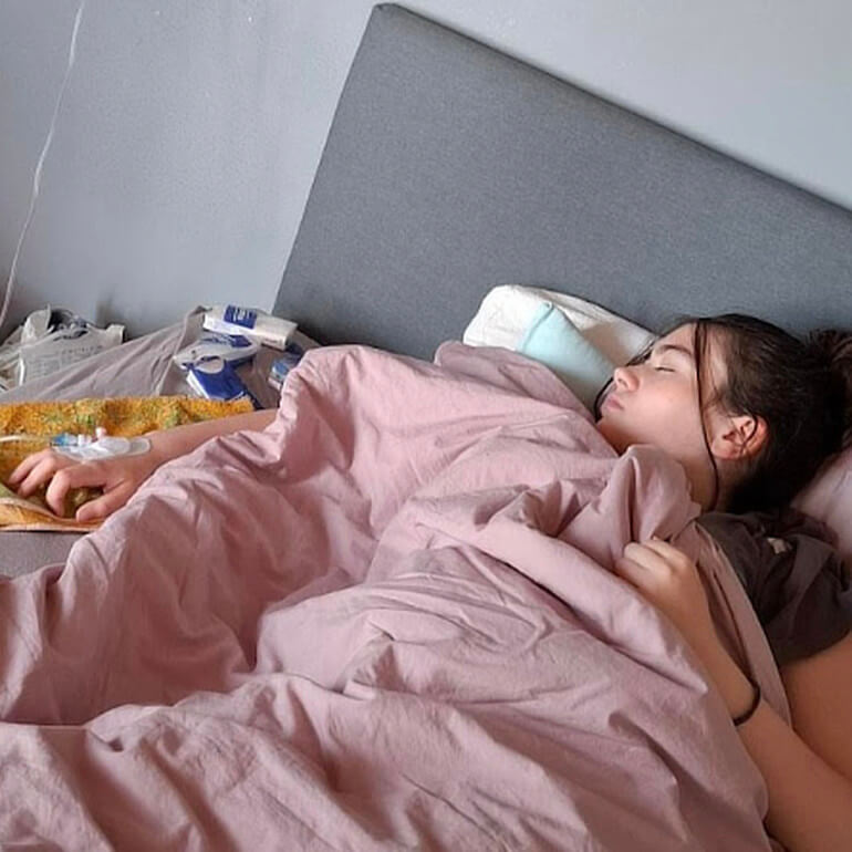 Rosi liegt mit geschlossenen Augen im Bett, in der Hand eine Infusion
